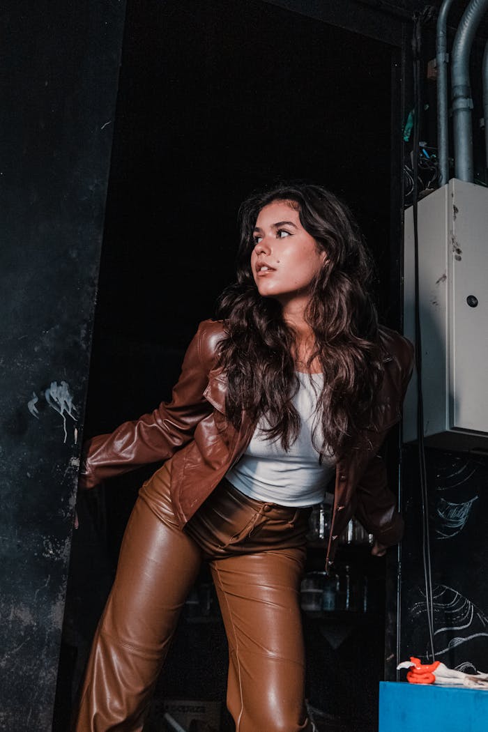 Brunette woman striking a pose in leather outfit with dramatic lighting.