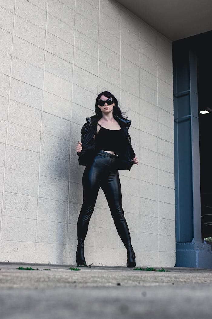 Stylish woman in black leather standing confidently against a white wall.