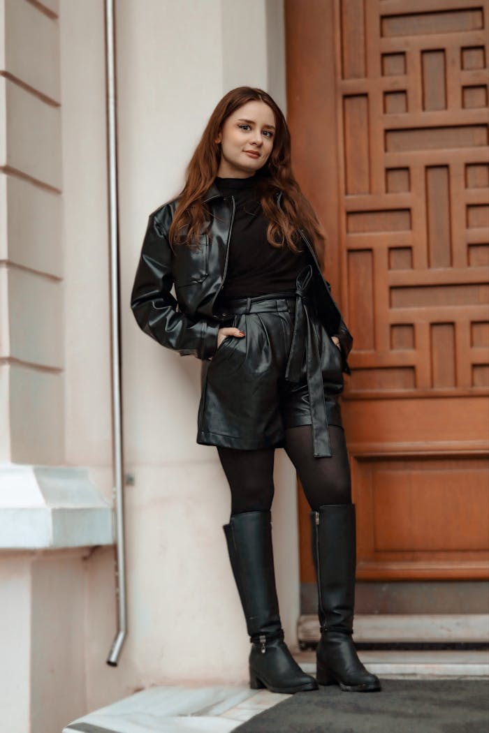Fashionable woman standing against wooden door in chic leather outfit.